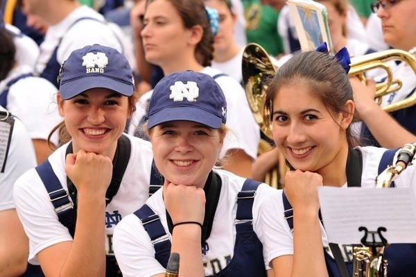 Three female members of the Notre Dame marching band pose with their fists underneath their chins.