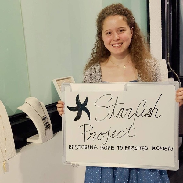 Smiling woman with curly brown hair holds a whiteboard: 'Starfish Project. RESTORING HOPE TO EXPLOITED WOMEN'.