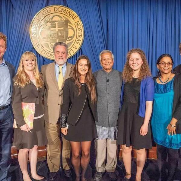 Eight diverse people smile before the gold Notre Dame seal and blue curtain.