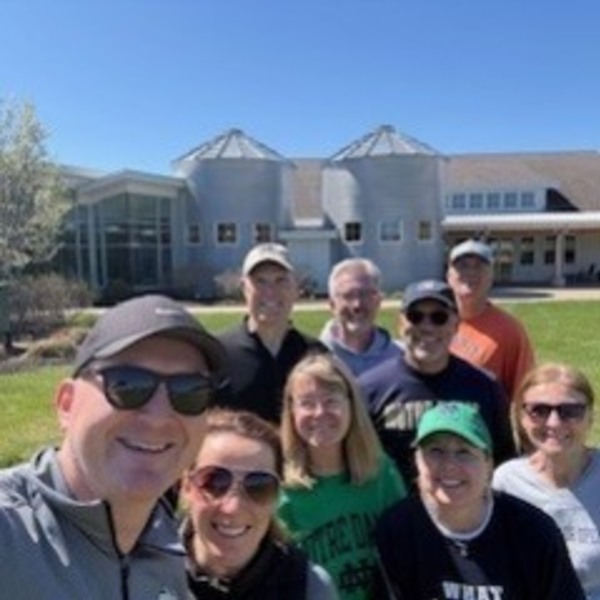 Nine smiling people, some wearing Notre Dame gear, take a selfie outside.